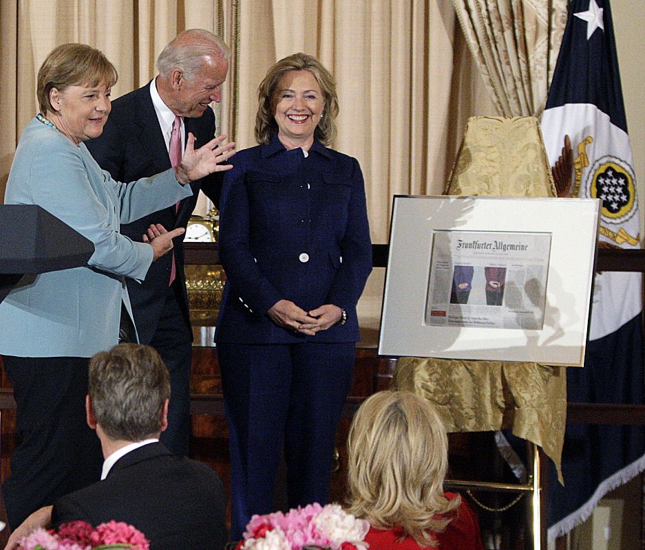 Merkel enseña un obsequio para la secretaria de Estado norteamericana, Hillary Clinton. Es una portada del diario Frankfurter Allgemeine que muestra a las dos políticas de cintura para abajo.