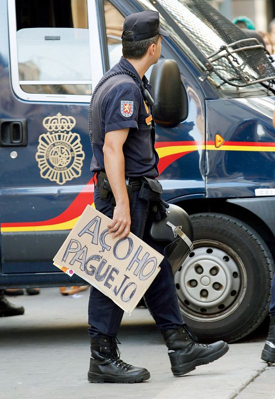 Un agente de la Policía Nacional sujeta un cartel en el que se puede leer, "Esto lo pago yo" durante las protesta del movimiento 15-M