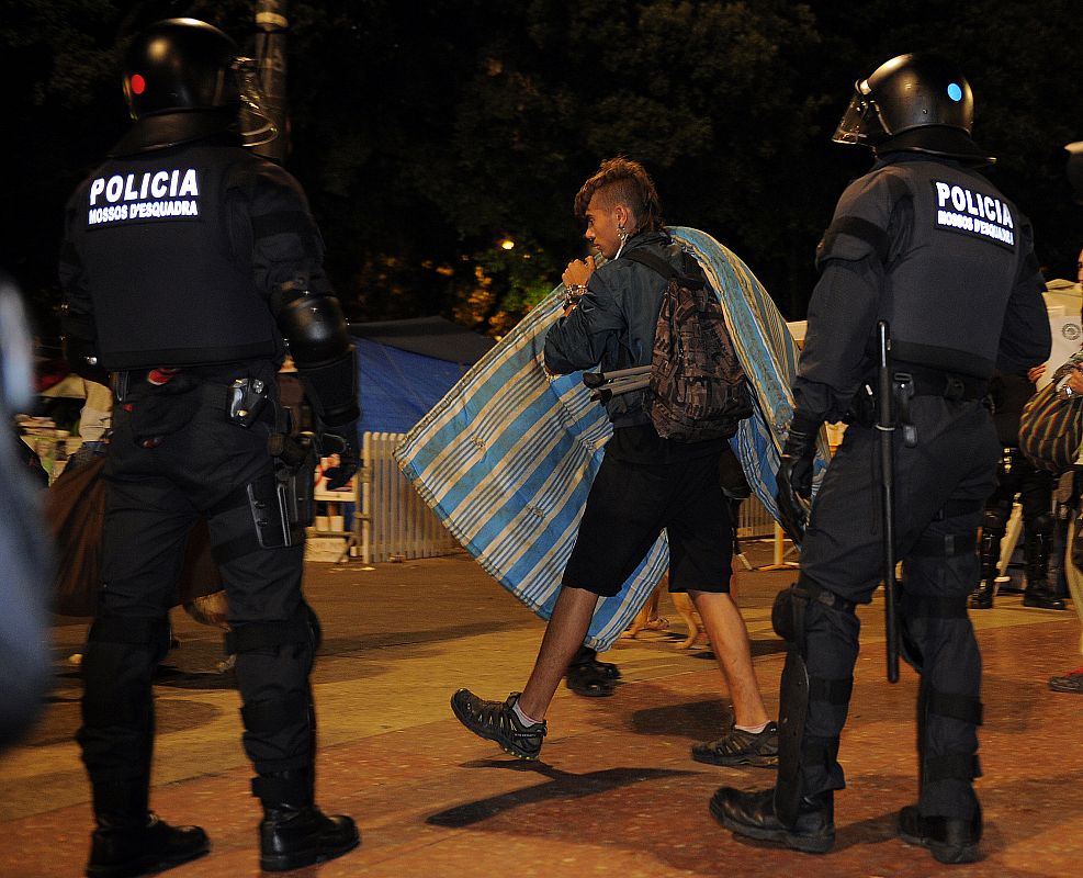 Un 'indignado' recoge su colchón ante la mirada de la guardia urbana de Barcelona
