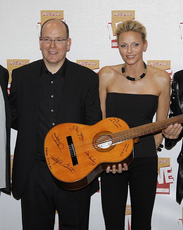 Monaco's Prince Albert II and his fiancee Charlene Wittstock pose with an autographed guitar presented by rock group 'The Eagles' before a concert at the Stade Louis II stadium in Monaco