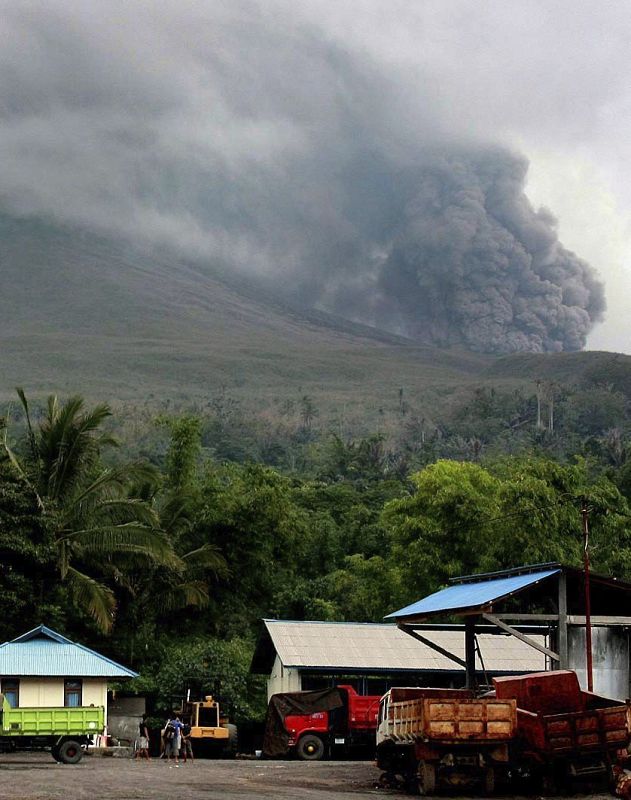 Varios trabajadores indonesios miran como el volcán Lokon arroja gases y cenizas