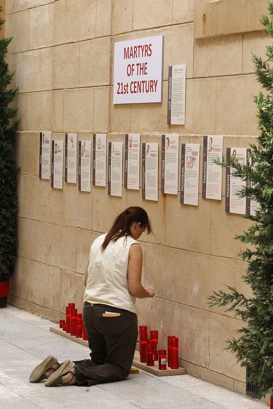 Una joven enciende unas velas en la sala donde se exhiben unos paneles que narran la historia de quince mártires de los últimos cincuenta años, dentro de la exposición fotográfica "Cristianos perseguidos hoy"