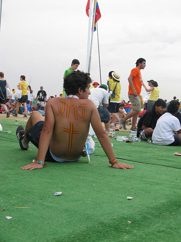 Un jóven, con las siglas de la JMJ en la espalda, espera la llegada del papa a Cuatro Vientos