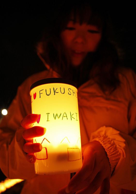 A woman holds a candle before placing it down to form the shape of "Praying, 3.11" at a candlelight event in Iwaki, Fukushima