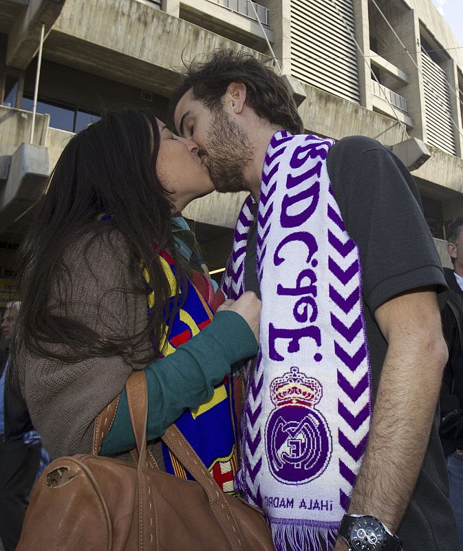 Una pareja de aficionados, ella del FC Barcelona y él del Real Madrid, se besan momentos antes de comenzar el partido