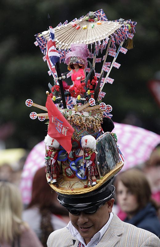 A man wears a hat with a doll figure of Britain's Queen Elizabeth as he walks on the banks of the River Thames in central London