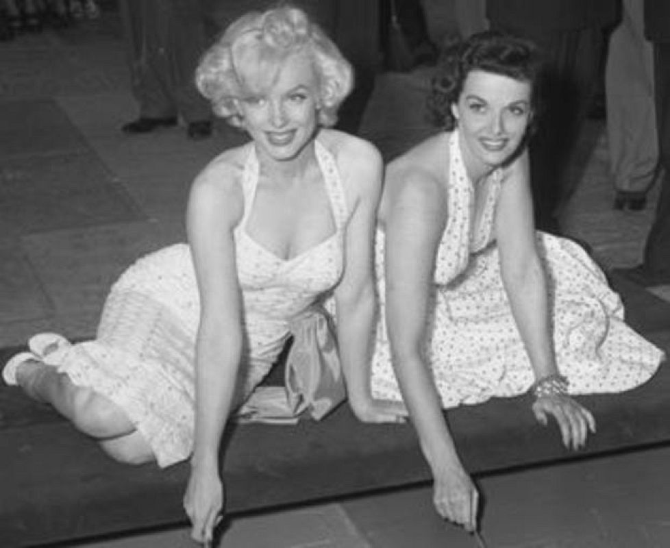 Marilyn Monroe y Jane Russell estampando sus huellas en el cemento en el Teatro Chino de Los Ángeles, California, en 1953. 