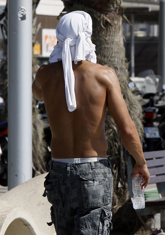 Un joven se tapa la cabeza con una camiseta en la playa de la Barceloneta para protegerse del calor