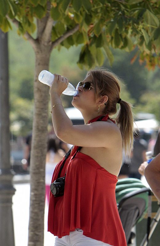 Una chica bebe agua mientras pasea por el parque del Retiro en Madrid