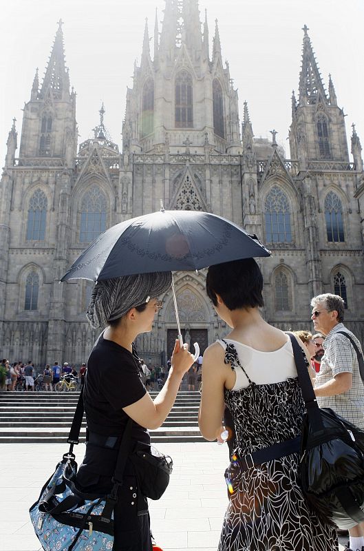 Unos turistas se protegen del sol con un paraguas frente a la catedral de Barcelona