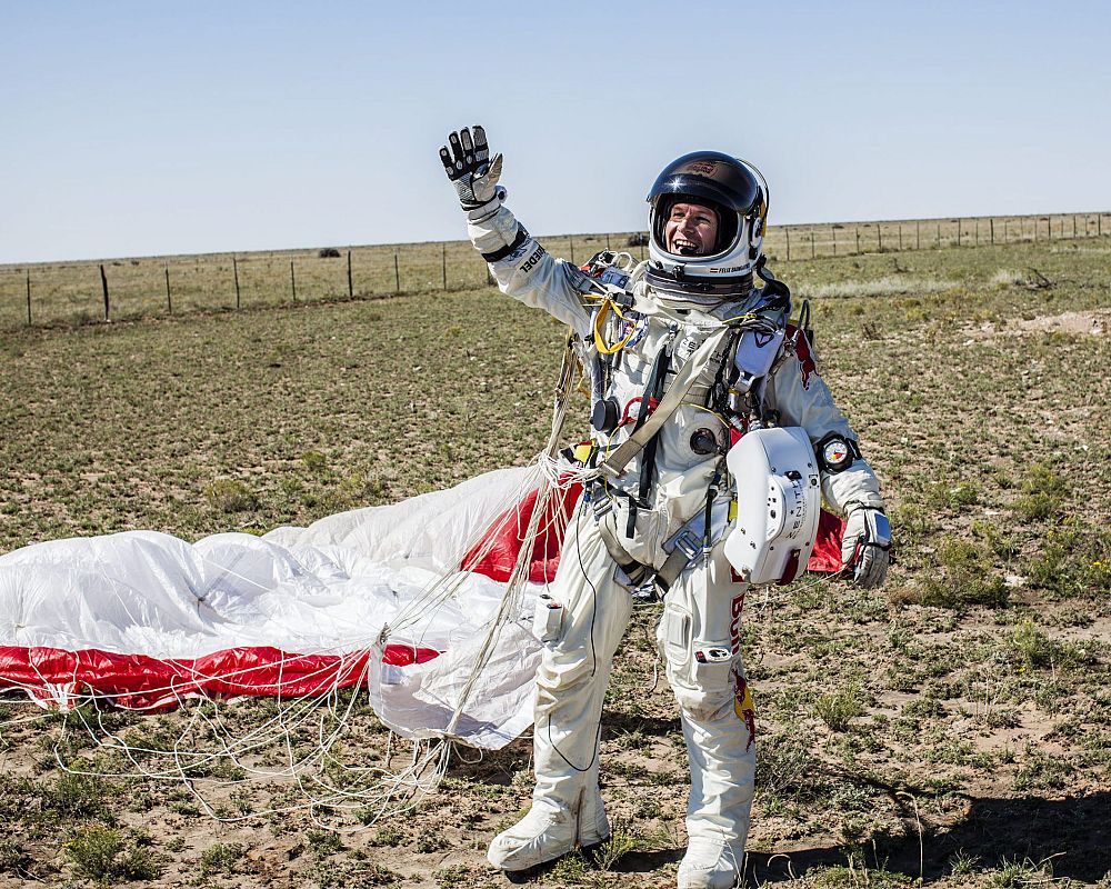 Baumgartner, como si fuera un hombre del espacio, saluda a su equipo tras conseguir con éxito superar su misión del mayor salto en caída libre de la historia y romper la barrera del sonido.