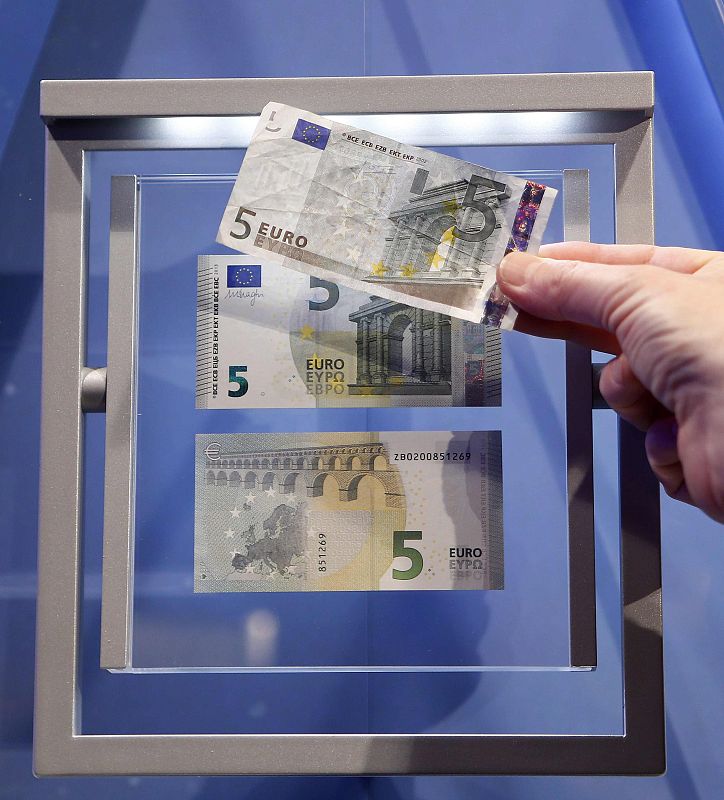 A journalist compares the new 5 euro note with an old one (top) during a ceremony with Draghi, President of the European Central Bank (ECB), in Frankfurt