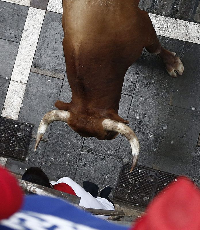 Un mozo se refugia de un toro en la calle Estafeta durante el último encierro de las fiestas