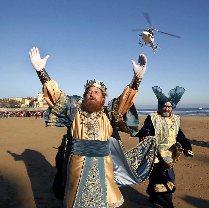 El rey Gaspar saluda a los niños tras descender de un helicóptero en la playa de San Lorenzo de Gijón,  después de décadas de llegar al puerto de la ciudad a bordo de la embarcación "Estrella de Oriente"