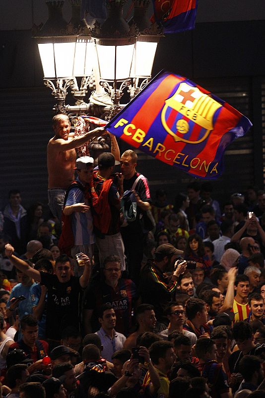 Un aficionado ondea una bandera del equipo azulgrana encaramado a la fuente en Barcelona.