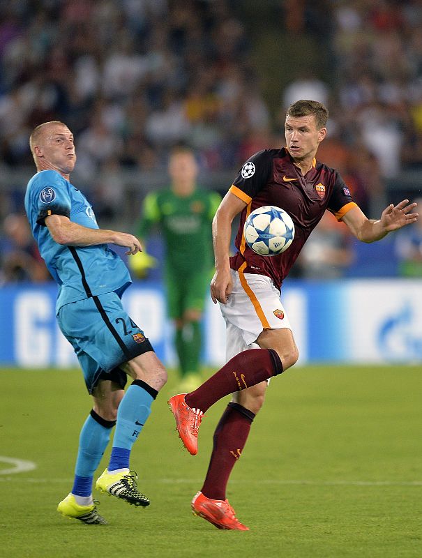 El bosnio Edin Dzeko, de la Roma, trata de superar al barcelonista Jeremy Mathieu