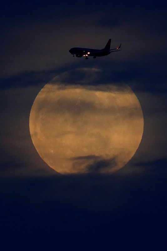 A full moon rises between clouds as a landing commercial jet approaches the airport before the start of a total lunar eclipse that is called a 'Super Blood Wolf Moon' in San Diego