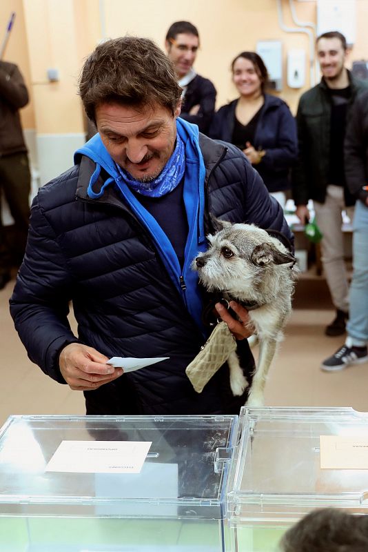 Un elector acompañado de su mascota deposita el sobre con las papeletas en una urna en el CEIP La Navata, en la localidad madrileña de Galapagar.