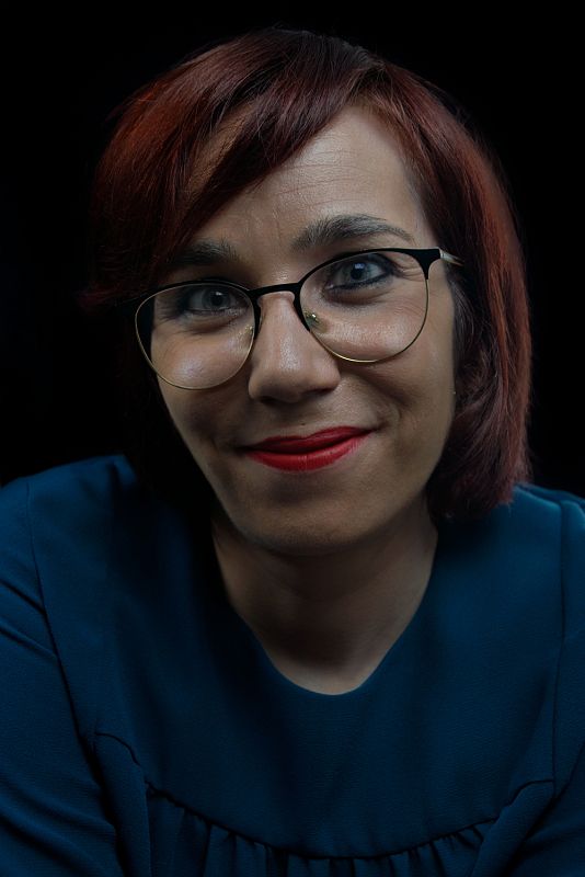 Ángeles sonríe. Lleva una blusa azul, gafas, los labios pintados de rojo y el pelo caoba.