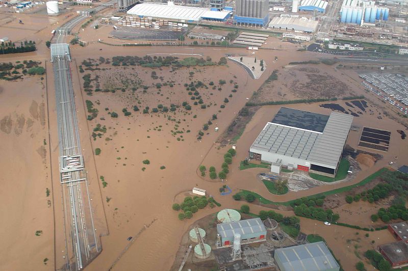 Vista aérea de una planta química inundada.  Agua marrón cubre el terreno, afectando carreteras, vías de tren y edificios industriales. Se observa una vía férrea elevada.