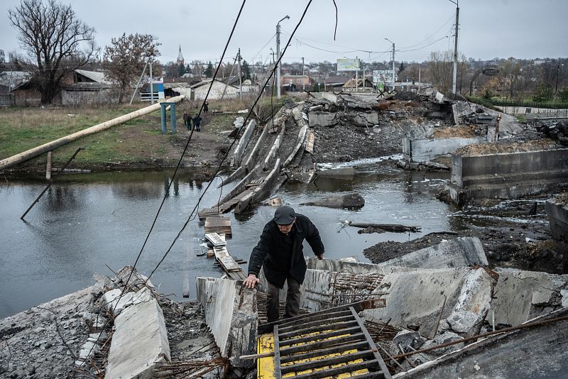Hombre caminando sobre las ruinas de un puente destruido.  Se observan escombros y el cauce del río.  Imagen desoladora.