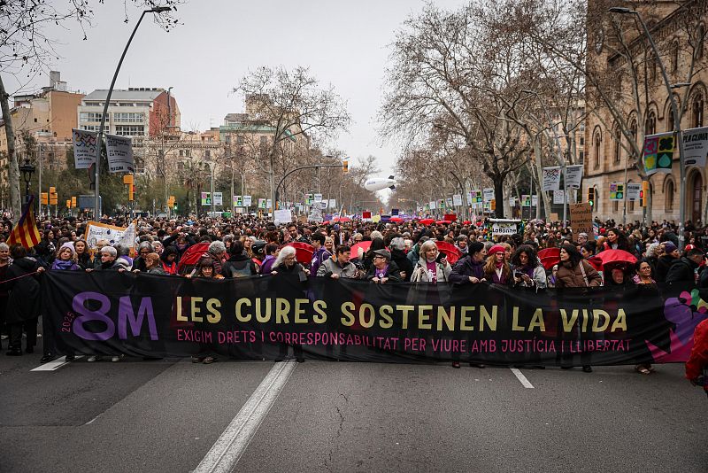 Multitud en manifestación del 8M 2023 en Barcelona. Gran pancarta negra con letras rosas y doradas: "Los cuidados sostienen la vida. Exigimos derechos y corresponsabilidad para vivir con justicia y libertad".  Marcha por avenida arbolada.