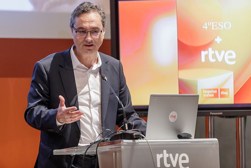 Hombre con traje y gafas da un discurso en atril con logo RTVE; pantallas muestran logos RTVE y textos "4º ESO + rtve" e "Impulsa Visión".