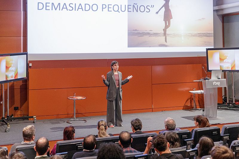 Presentación en un escenario con una joven gesticulando; la frase "DEMASIADO PEQUEÑOS" se proyecta en una pantalla grande, con el logo de RTVE en pantallas más pequeñas.