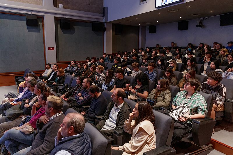 Auditorio con adolescentes y adultos sentados, presenciando una presentación o evento.  Los jóvenes se ubican en las filas superiores, los adultos en las inferiores.