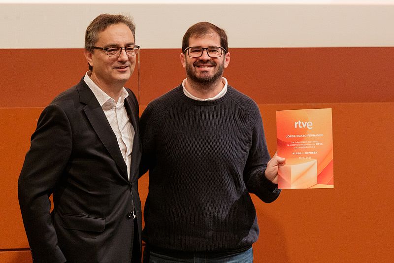 Entrega de un diploma a Jorge Díaz Ferrando en un evento. Un hombre en traje y otro con jersey posan para una foto con el diploma de RTVE.