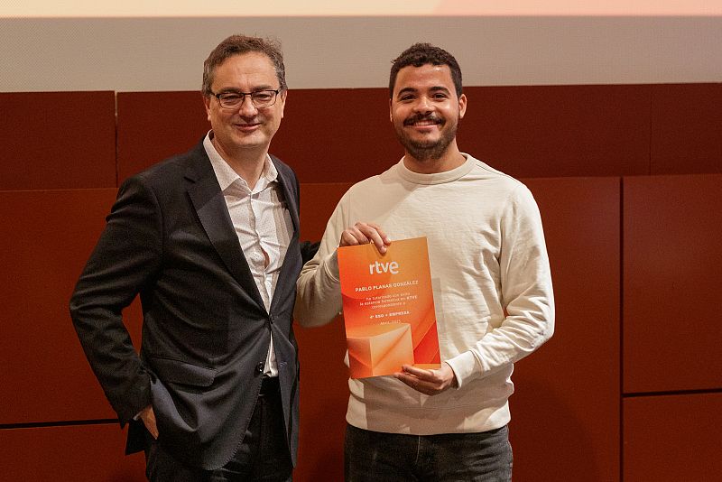Entrega de reconocimiento en una gala a Pablo Planas González por su participación en el programa '4º ESO + Empresa' de RTVE. El galardonado sonríe mientras recibe el premio de manos de un hombre en traje.