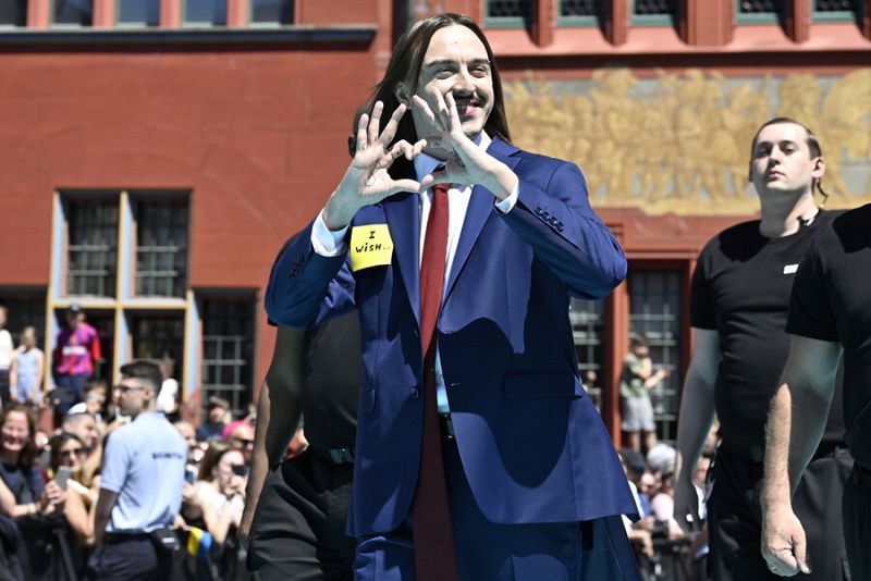 Käärijä en la alfombra turquesa de Eurovisión, traje azul, corbata roja, pegatina 'I wish', gesto de corazón, sonrisa.