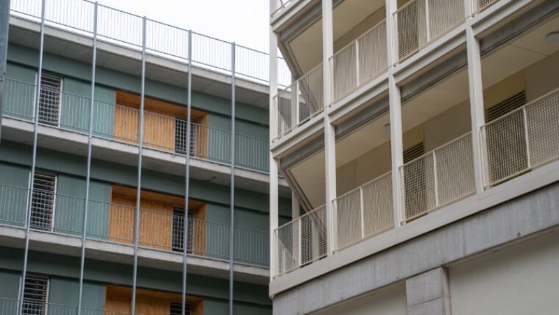 Edificios en construcción con fachadas verde oscuro y blanca, balcones con barandillas metálicas y aberturas con tablones de madera.