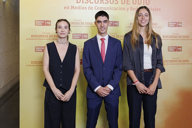 Tres personas posan en evento sobre discursos de odio en medios y redes sociales.  Logos de Impulsa Visión y RTVE presentes.  Asistentes con vestimenta formal.