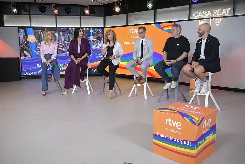 Grupo de seis personas en escenario ante pantalla mostrando desfile con bandera LGTBI+.  Textos visibles: "rtve Catalunya", "Barcelona", "CASA SEAT".