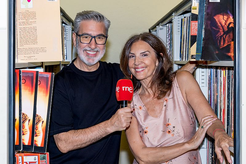 Carles Mesa y una mujer, con un micrófono de RNE, en un espacio con estanterías llenas de discos y libros.  Posible grabación de programa de radio.
