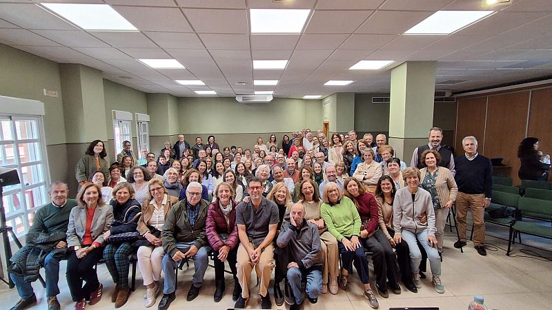 Un grupo numeroso de personas, mayoritariamente adultos y adultos mayores, posan para una fotografía en un salón con buena iluminación. Visten ropa casual y se aprecian sonrisas en sus rostros.