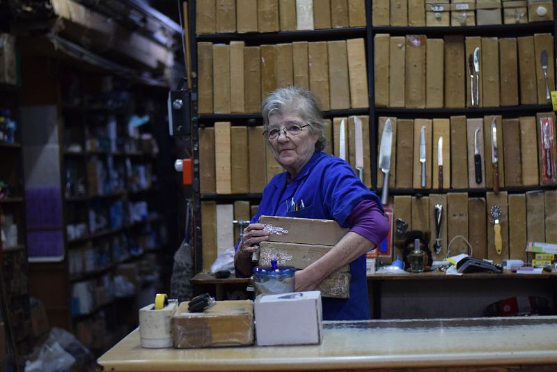 Alicia Molina, con gafas y camisa azul, recoge cajas en una ferretería. Detrás de ella, se aprecian estanterías repletas de cajas y utensilios.
