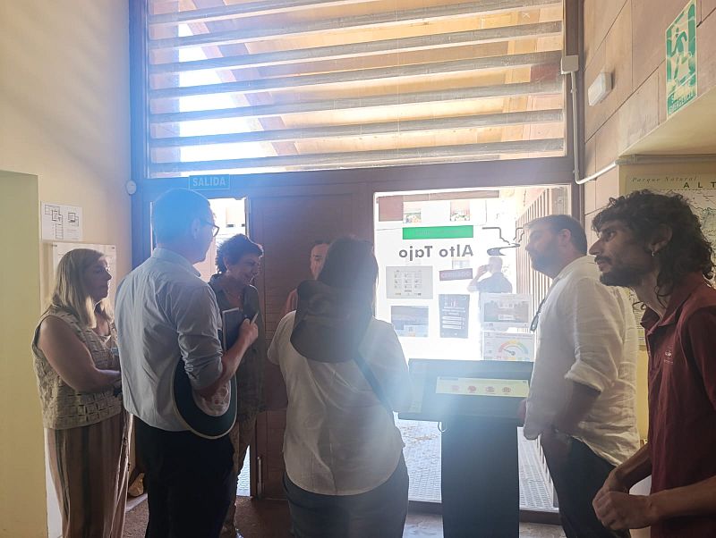 Grupo de visitantes en un centro de interpretación con cartel "Parque Natural ALTO TAJO" y señal de "SALIDA".