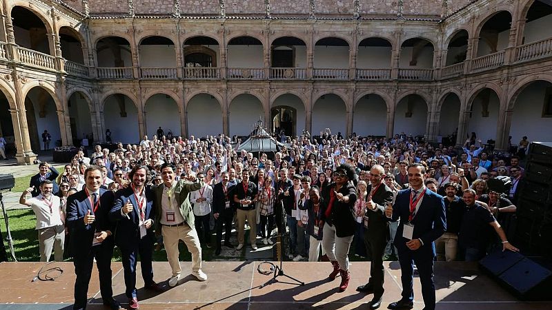 Foto de grupo al aire libre en un patio histórico con una multitud de asistentes y ponentes en una tarima celebrando el evento de emprendimiento.