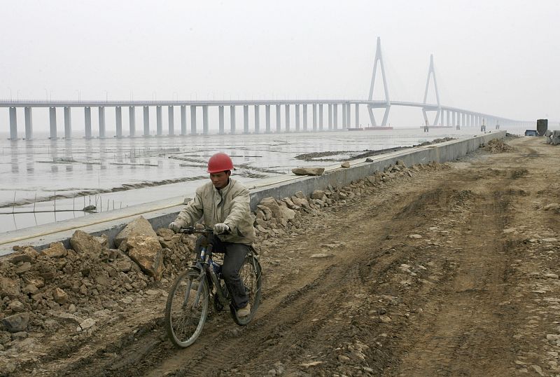 Worker cycles past the construction site of Hangzhou Bay Bridge in Ningbo