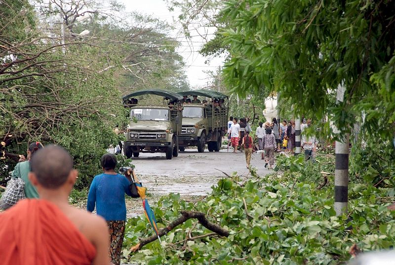 VARIOS CAMIONES MILITARES QUE INTENTAN ABRIRSE PASO ENTRE VARIOS ÁRBOLES EN EL SUELO DE UNA CALLE DE YANGON, BIRMANIA