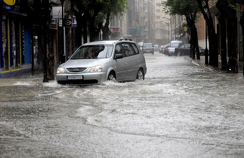 Un vehículo circula por una de las calles de Albacete que se encuentra inundada como consecuencia de las últimas lluvias caídas en la región manchega.