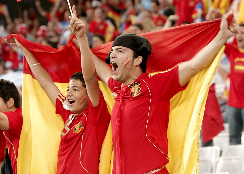 Varios hinchas españoles animan a su selección, con la bandera española como capa.