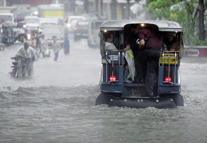 Varios peatones y motoristas se trasladan por una calle inundada por las lluvias tifónicas en la ciudad de Paranaque, al sur de Manila, Filipinas,