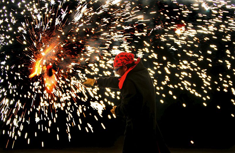 Un ciudadano baila y juega con fuego alrededor de una hoguera de San Juan instalada en el barrio de Sants de Barcelona, una de las miles que esta noche se encienden en toda Cataluña en conmemoración del solsticio de verano.