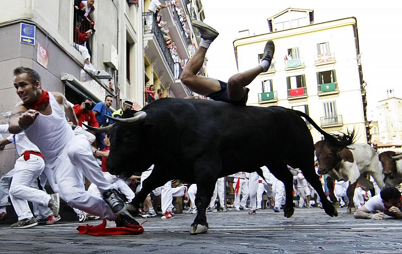 A runner falls on top of a fighting bull as they take the Estafeta curve during the third bull run of the San Fermin festival in Pamplona
