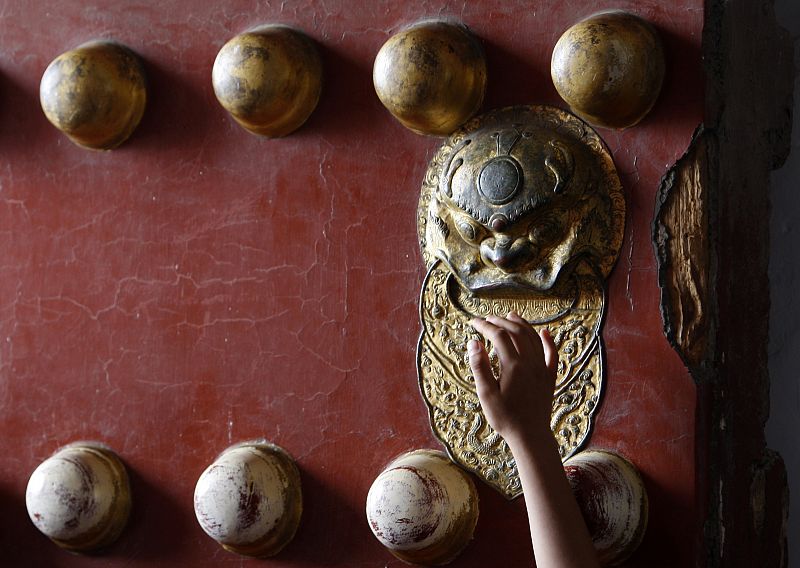 A visitor reaches up to touch the door of Tiananmen gate in Beijing as he enters it