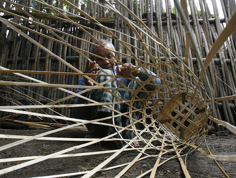 An ethnic Karen man weaves a bamboo basket at a stilted house in Mae La camp