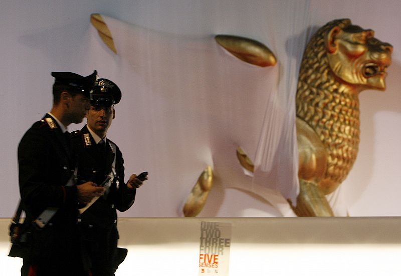 Two Carabiniers walk past a golden lion statue in front of the Cinema Palace in Venice